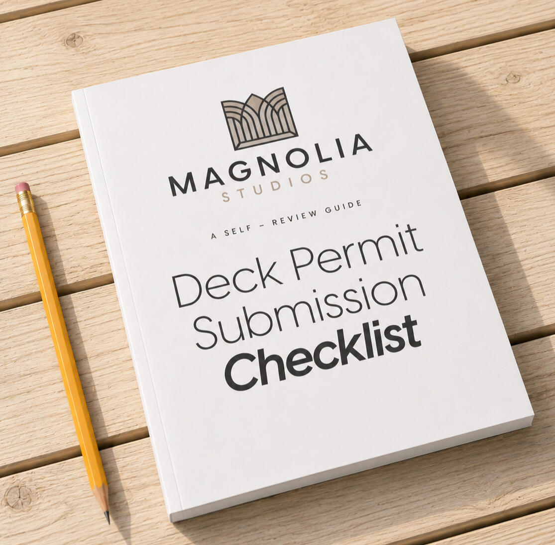 Mockup of the Magnolia Studios Deck Permit Submission Checklist booklet resting on a wood deck surface beside a pencil.